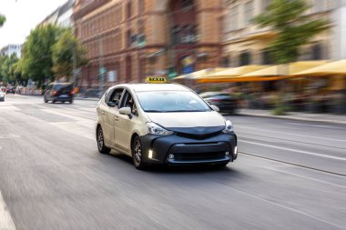 Açık renkli taksi hareketli bir şehir caddesi boyunca hareket bulanıklığı efektiyle ilerliyor, hızlı şehir dinamiklerini ve ulaşım hizmetlerini iletiyor.