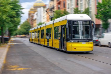 Sarı eklemli bir tramvay Berlin caddesinde hareket bulanıklığı ve tarihi binaların arka planında, ulaşım modernliğini mimari mirasıyla harmanlıyor..
