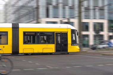 Sarı bir tramvay şehir kavşağında hareket bulanıklığı ile koşar, modern şehir yaşamının hızını ve enerjisini yakalar..