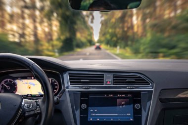 Modern araba navigasyon ve müzik ekranı aktif. Dinamik bulanıklık, manzaralı bir orman otoyolunda hız kazandırır.