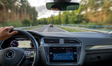 Orman yolunda bir sürücü, aracın içinden, aktif müzik ve GPS ile, hızı vurgulamak için görünür hareket bulanıklığıyla yakalanır..