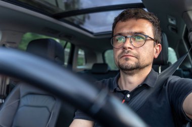 Modern bir araba kullanan odaklanmış bir adamın portresi. Doğal gün ışığı ve temiz bir kamara tasarımı kontrol ve konsantrasyonu vurguluyor..