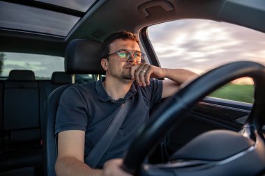 Düşüncelere dalmış bir adam, gün batımı ışığı ve araba penceresinin dışında hareket bulanıklığı. Sahne, iç gözlem ve seyahat havasını yansıtıyor..