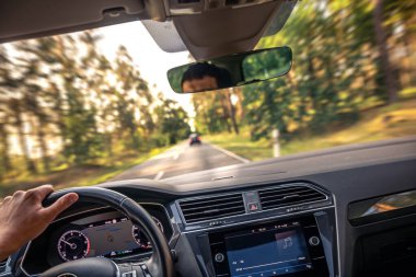 Pencerenin dışında hareket bulanıklığı olan, hızı vurgulayan, ekranda müzik ve direksiyonda sürücü eli olan bir arabanın içi.