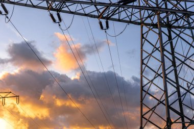 Yüksek voltajlı bir kule silueti ve elektrik hatlarıyla çarpıcı bir gün batımı. Gökyüzü renkleriyle çelişiyor..