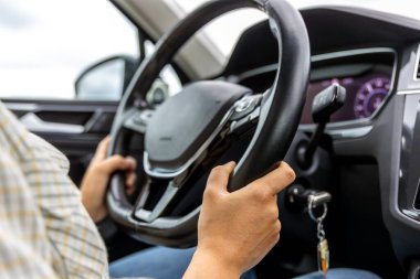 Arka planda gösterge paneli olan modern bir arabanın direksiyonunu tutan bir sürücünün yakın çekimi..