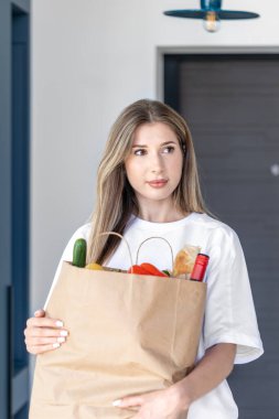 Girişte elinde kese kağıdıyla duran genç bir kadın. Modern bir ortamda çevre dostu paketleme ve bilinçli alışveriş.