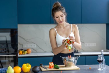 Bir kadın şık bir mutfakta kevaşeye kesilmiş sebze ekliyor. Temiz yemek ve sağlıklı günlük rutin bir kutlama düzenliyor..