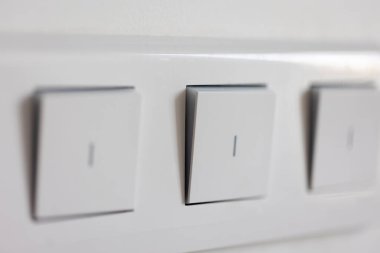 Beyaz bir duvardaki üç düğmeli panelin yakın görüntüsü, yumuşak ışık ve temiz çizgiler. Minimalist tarzda modern elektrik donanımı.