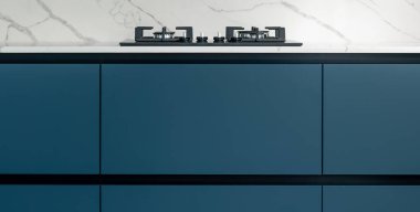 Kapalı mavi dolabın üstündeki gaz aşçısının geniş görüşü. İnce bir tezgah bandı ve taş kaplama minimalist estetiği vurguluyor.