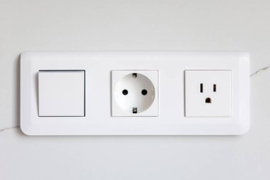 Beyaz duvar bloğu, bir anahtar ve pürüzsüz bir yüzeyde farklı standartlarda iki soket. Modern minimalist tarzda temiz bir elektrik tesisatı.