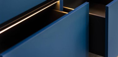 Sıcak LED parıltısı ve derin gölgeleri olan elsiz çekmeceler dar açıda. Çapraz ışık çizgisi, minimalist ve modern mutfak havasını vurgular..