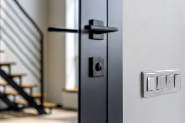 Siyah cam kapı kolunun yan görünüşü ve duvarda dört beyaz düğme, gün ışığı, keskin kenarlar ve enerji tasarrufu yaşam tarzına bir kafa sallama..