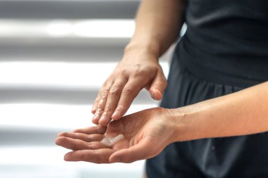 Avuç içlerindeki kremi pencerenin yanında ısıtan el açıları. Moda minimalizmi ile günlük kişisel bakım ritüeli.