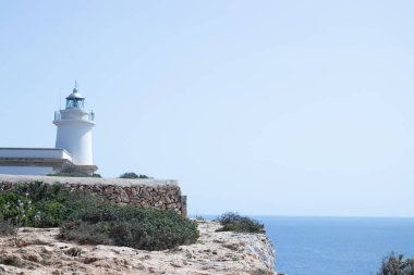 Dağın tepesine tünemiş el değmemiş beyaz bir deniz feneri, berrak mavi bir deniz manzaralı. Beyaz yapı ve canlı mavi sular arasındaki çarpıcı zıtlık dingin bir güzellik manzarası yaratır. Seyahatle ilgili konular için ideal