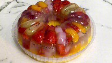 Sağlıklı meyveli puding. Puding vanilya jölesi, mango suyu ve taze çilek, üzüm, kivi, mandalina portakalı ve hindistan cevizi jölesi (nata de coco) ile doldurulur. Beyaz mermer mutfak masasında servis edildi. 4K