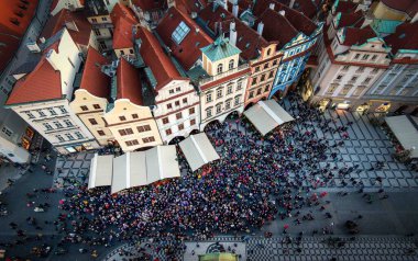 Kalabalık bir şehir meydanında insanların yoğun bir şekilde toplandığı bir hava perspektifi, bireylerin yürüme, konuşma ve tarama gibi çeşitli faaliyetlerde bulundukları bir ortam..