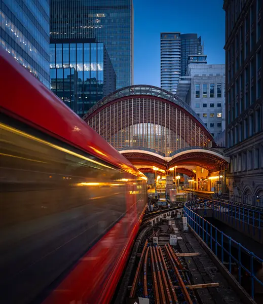 Parlak bir Londra metro kırmızı treni gece saatlerinde hareketli bir şehir manzarasında pürüzsüzce süzülüyor. Varlığıyla çevreyi aydınlatıyor.