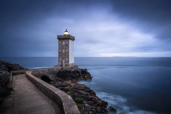 Huzurlu ve pitoresk bir deniz feneri, kasvetli bir gökyüzü ve Brittany Fransa 'da sakin bir deniz tarafından çerçevelenmiş kayalık sahilde görkemli bir şekilde duruyor.