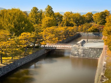 Canlı yapraklar ve sakin suyla çevrili tarihi bir Japon şatosunun çarpıcı sonbahar manzarası..