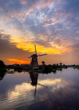 Üç yel değirmeni renkli bir günbatımı gökyüzüne karşı durmaktadır. Seyirciye en yakın yel değirmeni, bir kanalın durgun suyuna yansıyarak resim gibi bir manzara yaratıyor..
