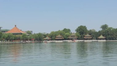 Sakin bir göl manzarası, berrak mavi gökyüzüne karşı geleneksel Çin mimarisini sergiliyor.