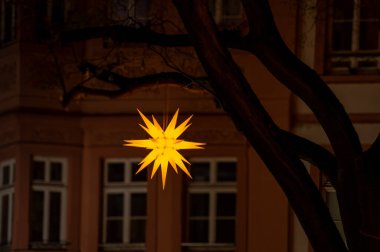 Canlı sarı bir yıldız süslemesi, gece bir binanın karanlık zeminine karşı aydınlatılır. Katıksız karşıtlık, neşeli atmosferi vurguluyor ve samimi bir ortam yaratıyor..