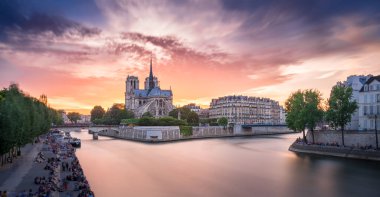 Muhteşem günbatımı, Notre Dame ve Seine Nehri 'nin üstündeki gökyüzünü aydınlatıyor. Paris' teki sakin bir akşamda, insanlar nehir kıyısında boş vakitlerin tadını çıkarıyorlar..