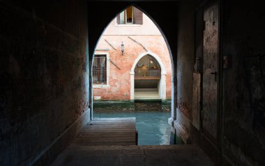 Venedik 'te sakin bir kanal açmak için dar bir geçit açılıyor. Yumuşak sabah ışığı yıpranmış duvarları ve durgun suyu aydınlatır ve huzurlu bir atmosfer yaratır..