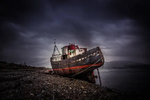 Karanlık çökmek üzere olan kara bulutlarla çevrili terk edilmiş bir gemi kayalık bir kıyı şeridinde duruyor. Durgun su sahnenin kasvetli atmosferini yansıtıyor, nostalji duyguları uyandırıyor..