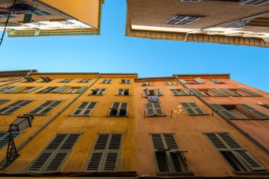 Parlak sarı ve pembe pencereli binalar açık mavi gökyüzünün altında büyüleyici bir manzara yaratıyor. Mimari canlı bir şehir atmosferinin özünü yakalıyor..