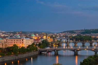 Alacakaranlık Prag 'ı aydınlatmakta, Vltava Nehri boyunca tarihi binalar ve köprüler sergilenmektedir..
