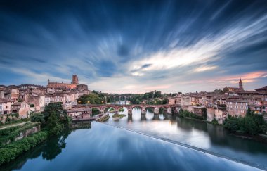 Albi 'deki sakin nehre bakan tarihi yapılar, sudan geceye dramatik bir gökyüzü geçişi olarak yansıyor. Atmosfer bu çarpıcı yerin güzelliğini vurguluyor..