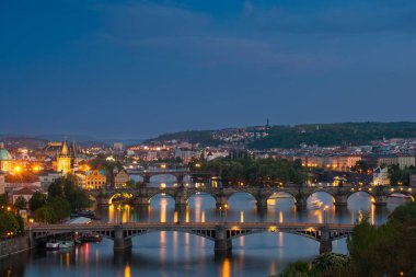 Prag 'ın çarpıcı bir manzarasında akşam gökyüzüne karşı birden fazla köprü var. Vltava Nehri şehrin altın ışıklarını yansıtarak sakin bir atmosfer yaratır..