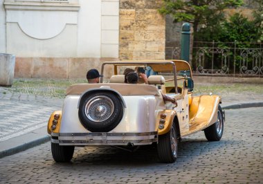 Prag 'da bir kaldırım taşı caddesi boyunca park edilmiş klasik bir üstü açık araba parlak gümüş ve sarı dış görünüşünü sergiliyor. Çevreleyen mimari ve yeşillik sahneyi tamamlıyor..