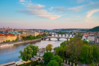 Huzurlu Vltava Nehri Prag boyunca akar, güneş batarken yemyeşil ve zarif mimari ile çevrili, tarihi köprüler ve binalar üzerinde altın bir parıltı bırakır..