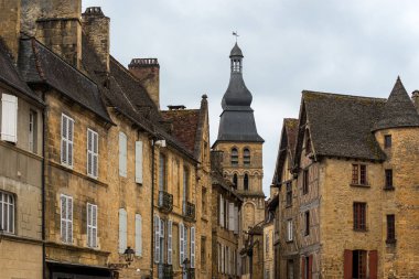 Ziyaretçiler, tarihi taş binalarla çevrili Sarlat-la-Caneda 'nın büyüleyici sokaklarında geziniyorlar. İkonik kule bulutlu gökyüzünün ortasında dikiliyor ve güzel bir manzara yaratıyor..