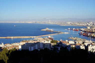 Cezayir Limanı 'ndaki Akdeniz' in geniş bir alanı, şehrin hareketli ufuk çizgisi ön planda belirgin bir şekilde gösterilerek çarpıcı bir kontrastla karşılaşılabilir..