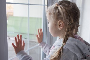 Little cute kid looking through the window. Concept of kids loneliness, soft focus background