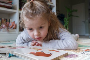 Little cute girl reading a book in the room, soft focus background. Education at home concept.