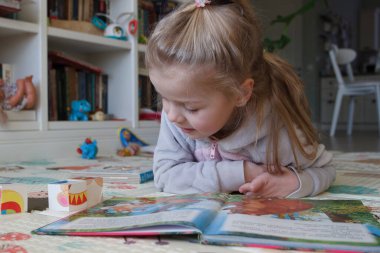Little cute girl reading a book in the room, soft focus background. Education at home concept.