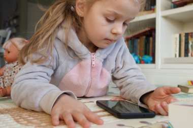 Little cute child holds a smartphone with a green screen. Concept of education online. Little kid with toys in the playroom