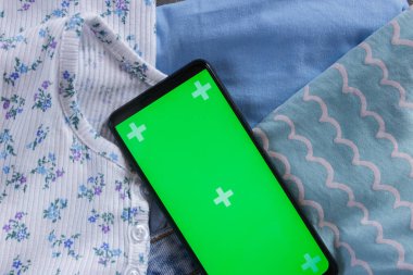 Farklı kıyafetler ve yeşil ekranlı bir akıllı telefon. Seyahat ya da online alışveriş kavramı