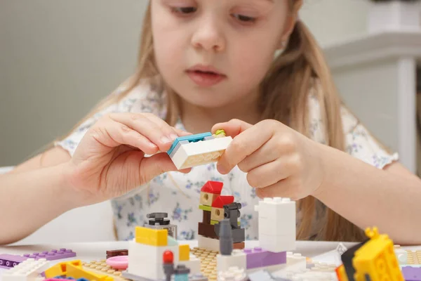Child builds with constructor bricks, plays with toys, soft focus background