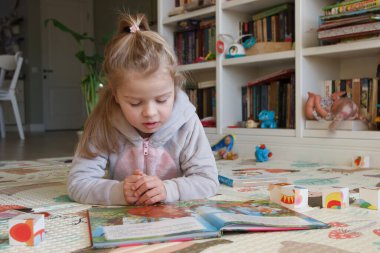 Little cute girl reading a book in the room, soft focus background. Education at home concept.