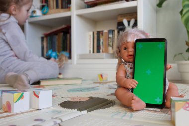 Smartphone with a green screen. Concept of education online. Little kid with toys in the playroom