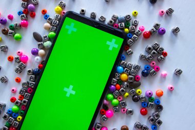 Yeşil ekranlı akıllı telefon ve üzerinde numaralar ve semboller olan farklı renkli boncuklar, üst görünüm