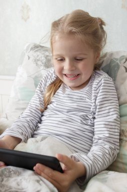Küçük şirin bir çocuk elinde akıllı bir telefonla yatakta yatıyor. Evde eğitim kavramı