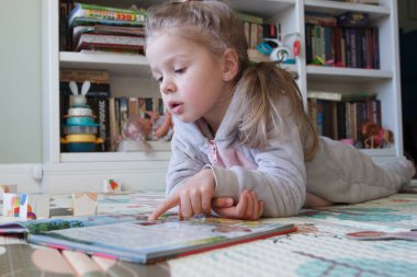 Little cute girl reading a book in the room, soft focus background. Education at home concept.