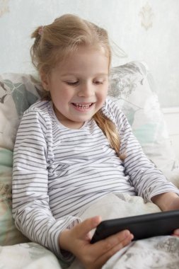 Küçük şirin bir çocuk elinde akıllı bir telefonla yatakta yatıyor. Evde eğitim kavramı